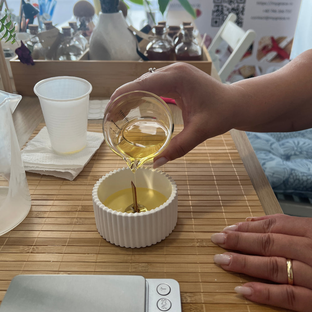 Cursantă turnând ceară lichidă în recipientul ceramic - sesiune practică de realizare a lumânărilor parfumate